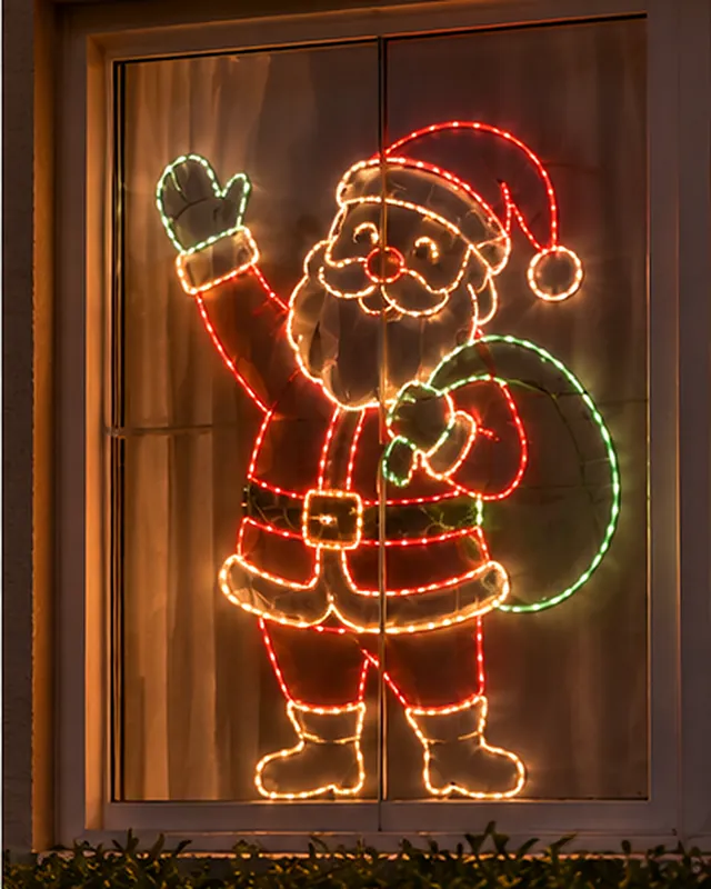 Papai Noel acenando com o saco de presentes, em contorno iluminado vermelho, branco e verde, fixado em uma janela
